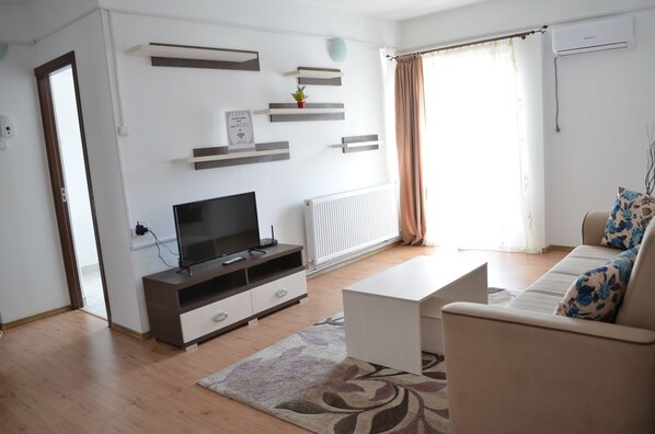 A modern living room with a flat-screen TV, a white sofa, and a coffee table. There are built-in shelves and a radiator on the wall. - Alexys Residence 6 (Iasi)