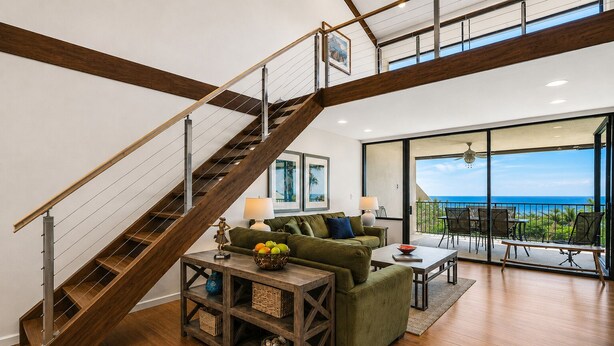 Una sala de estar moderna con una escalera de madera, un sofá verde, una mesa de centro y un balcón con vista al océano.