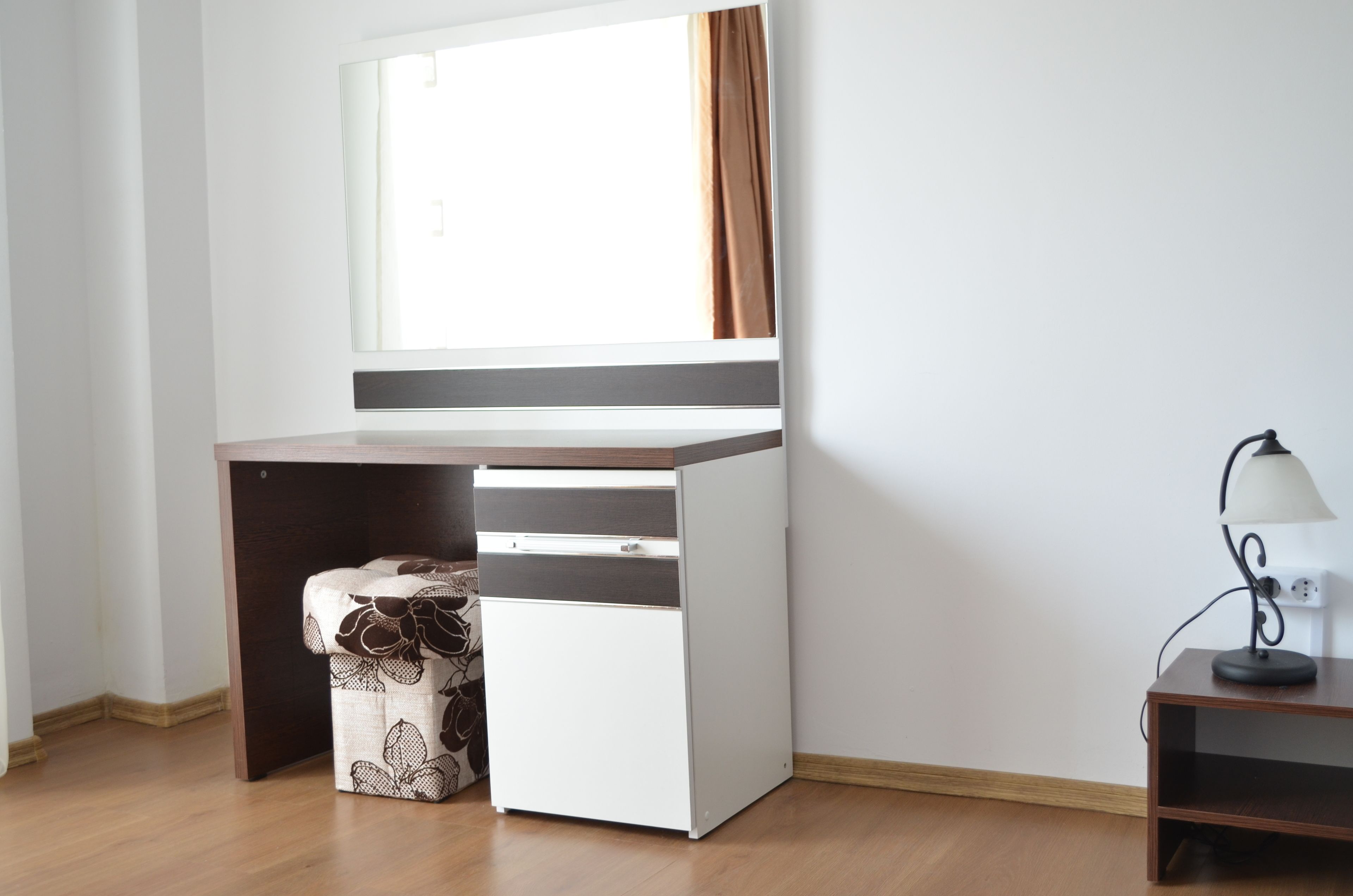 Ein kompakter, moderner Raum mit Schreibtisch und Stuhl, einem kleinen Tisch mit Lampe und einem fenster mit Vorhängen.