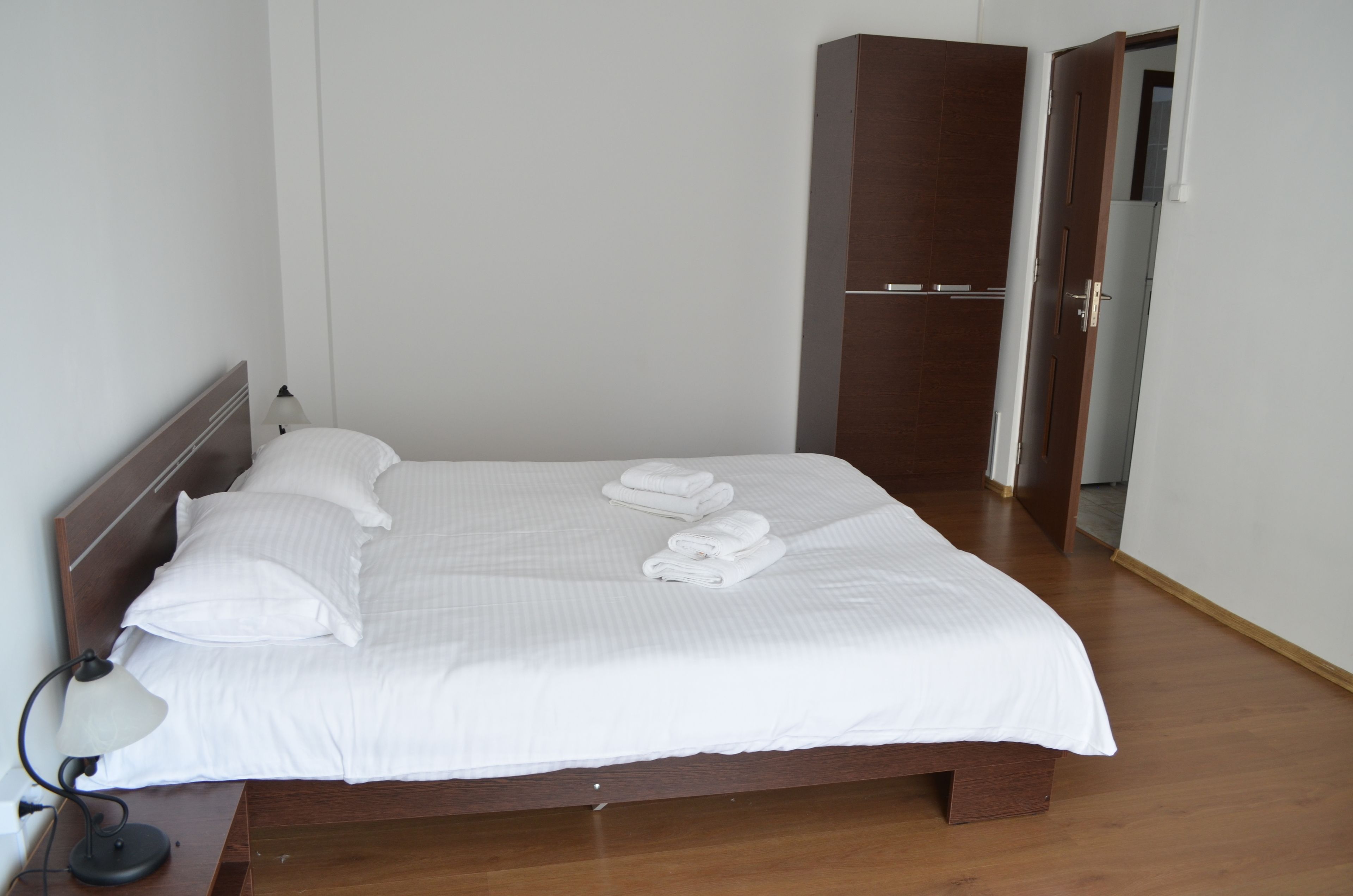 A neatly made bed with white linens and towels, a bedside lamp, and a wooden wardrobe in a hotel room.