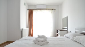 A hotel room with a neatly made bed, a desk with a chair, a mirror, and an air conditioning unit. - Alexys Residence 7 (Iasi)