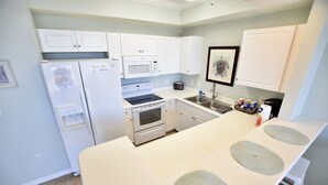 Une cuisine moderne avec des meubles blancs, un réfrigérateur, un four à micro-ondes, une cuisinière et un évier.