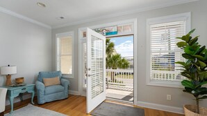 Une pièce avec un fauteuil bleu, une petite table d’appoint avec une lampe, une plante et une vue sur un balcon agrémenté de palmiers.
