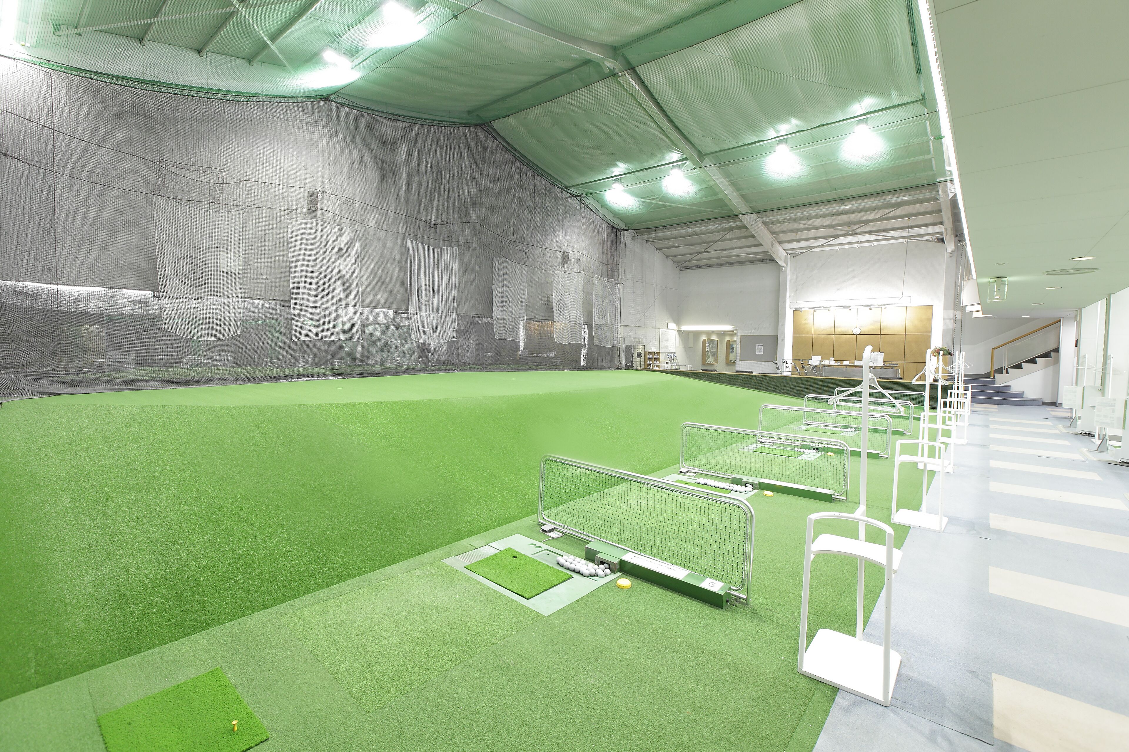 An indoor sports facility with artificial turf, target areas, and a seating area with a staircase.