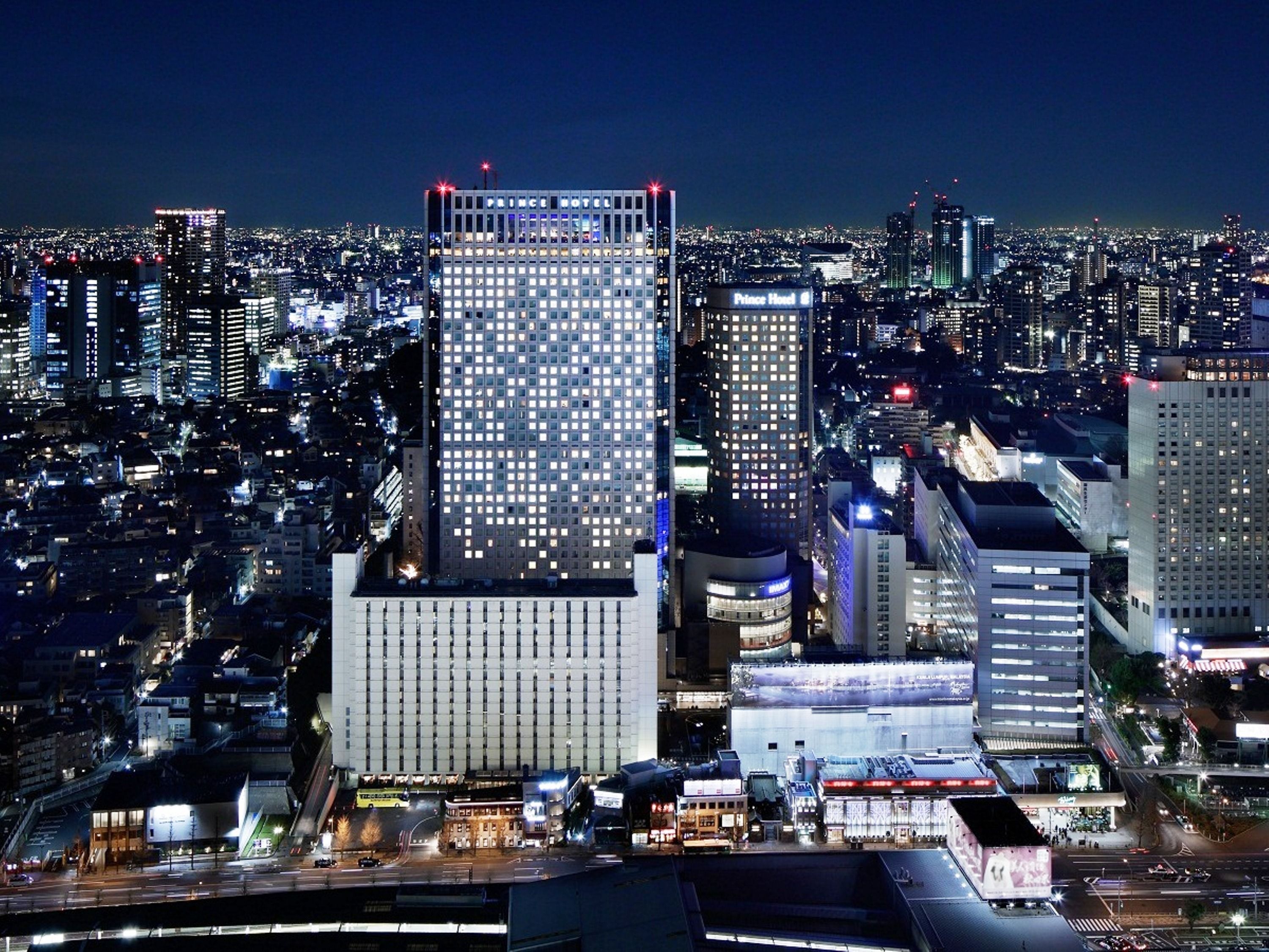 Un hotel moderno de gran altura con una fachada de ventanas enrejada, un letrero llamativo y vistas de la ciudad iluminada por la noche.