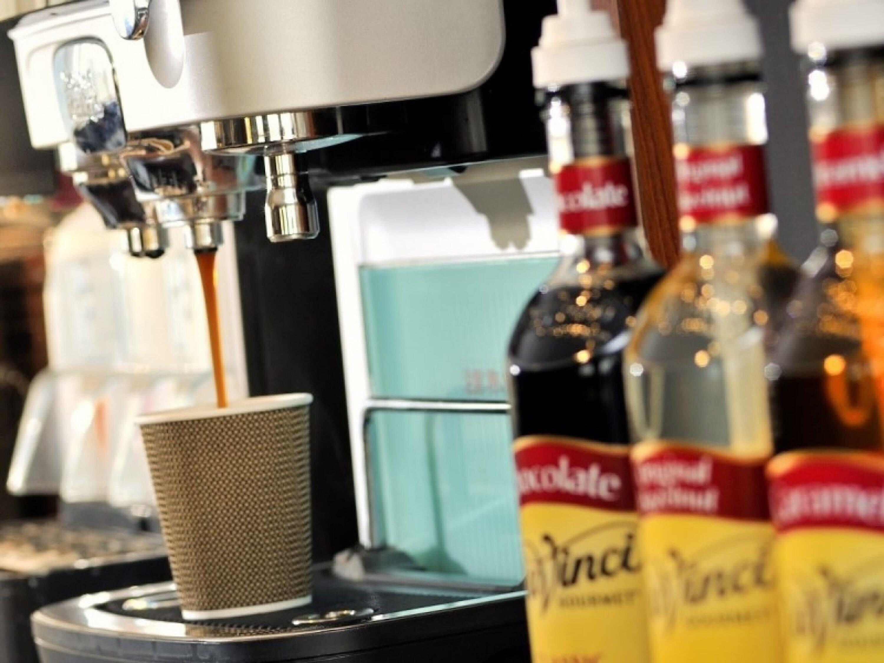 A coffee machine dispensing coffee into a cup, with bottles of wine and other beverages in the background.