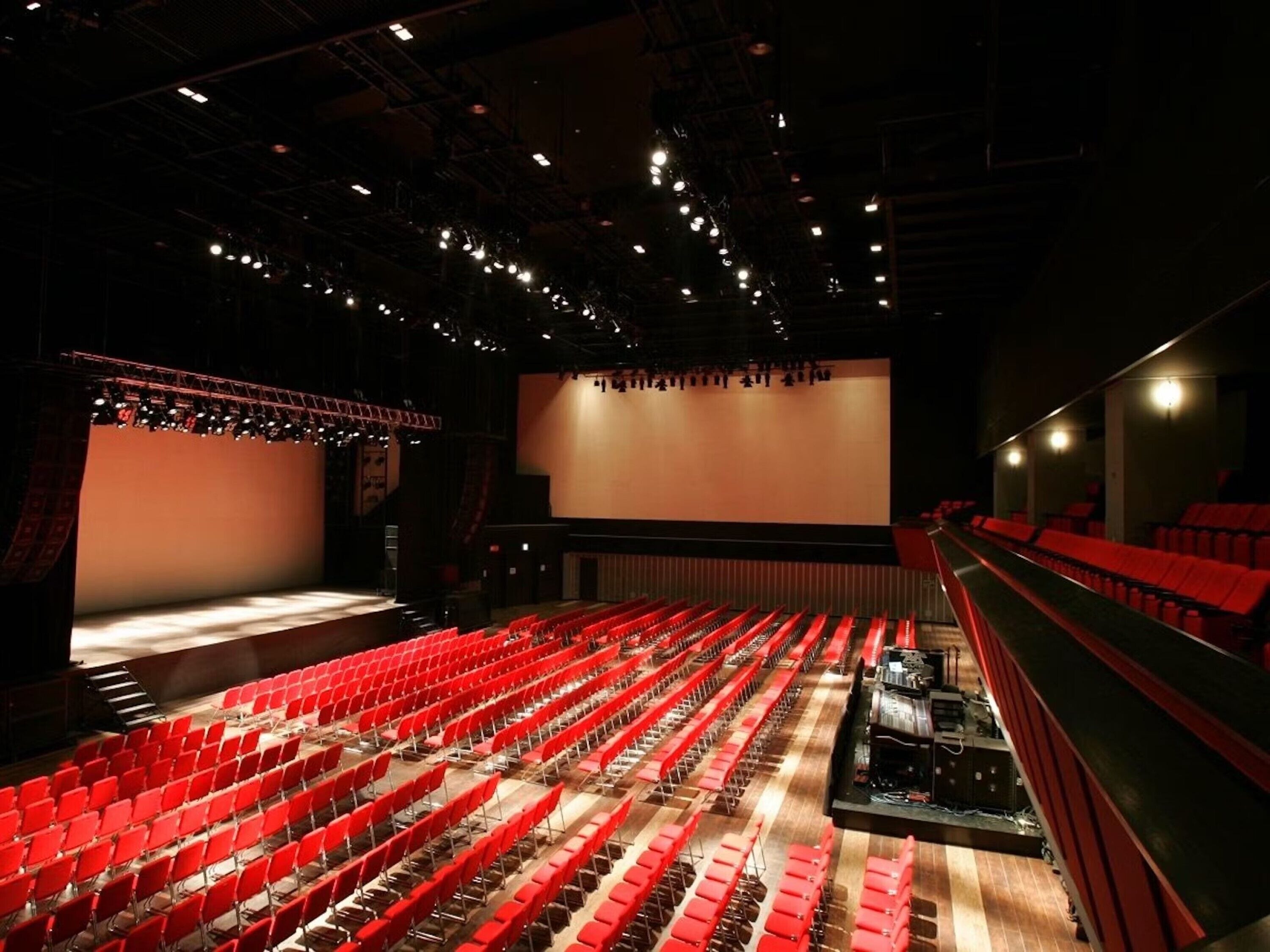 Une salle de spectacle avec des rangées de sièges rouges, une scène et un balcon.