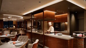 A modern restaurant with a chef preparing food, a bar area, and a dining section with tables and chairs. - Shinagawa Prince Hotel N Tower (Tokyo)