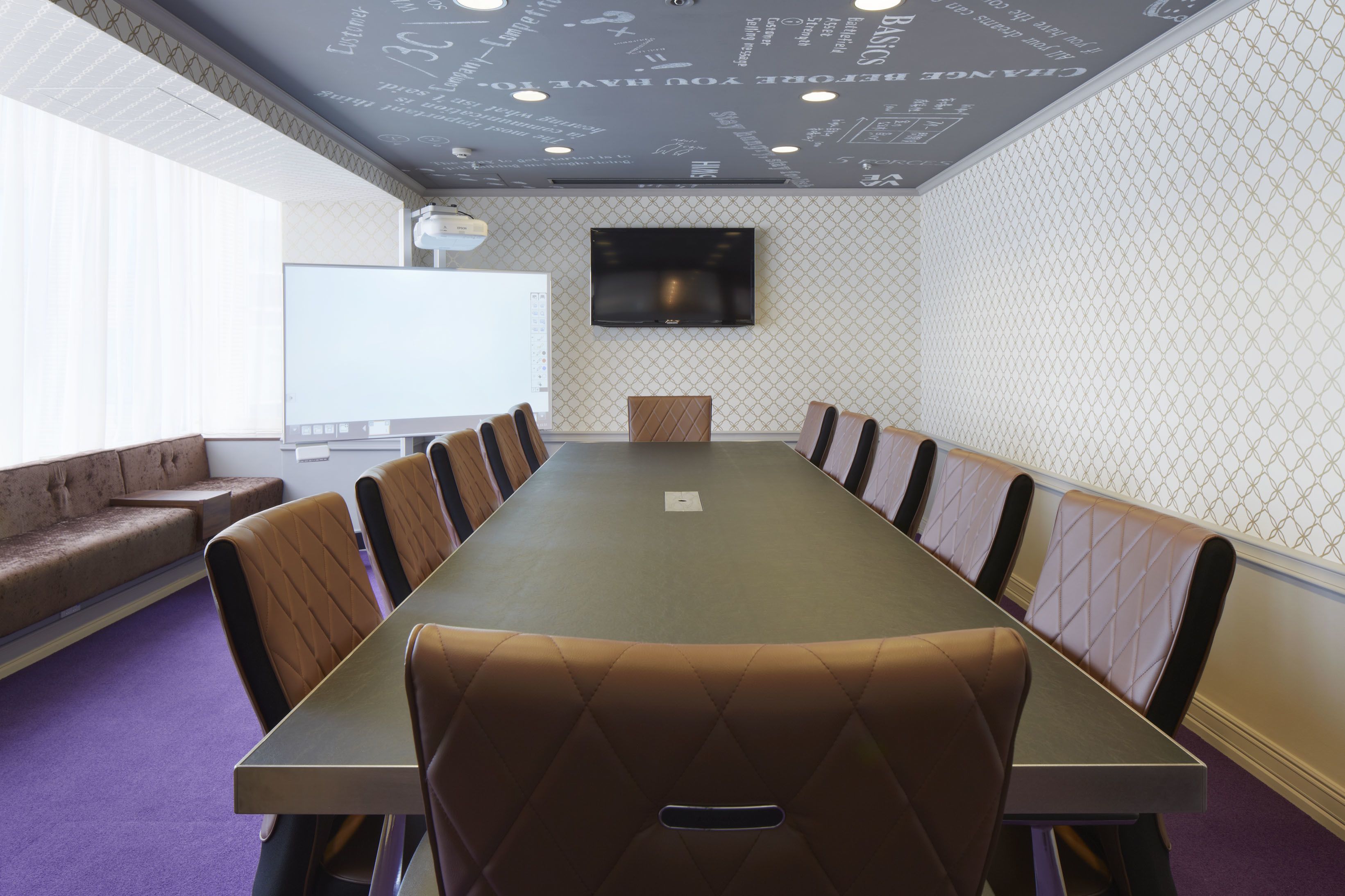 Une salle de conférence avec une longue table, des chaises confortables, un tableau blanc et un téléviseur à écran plat fixé au mur.