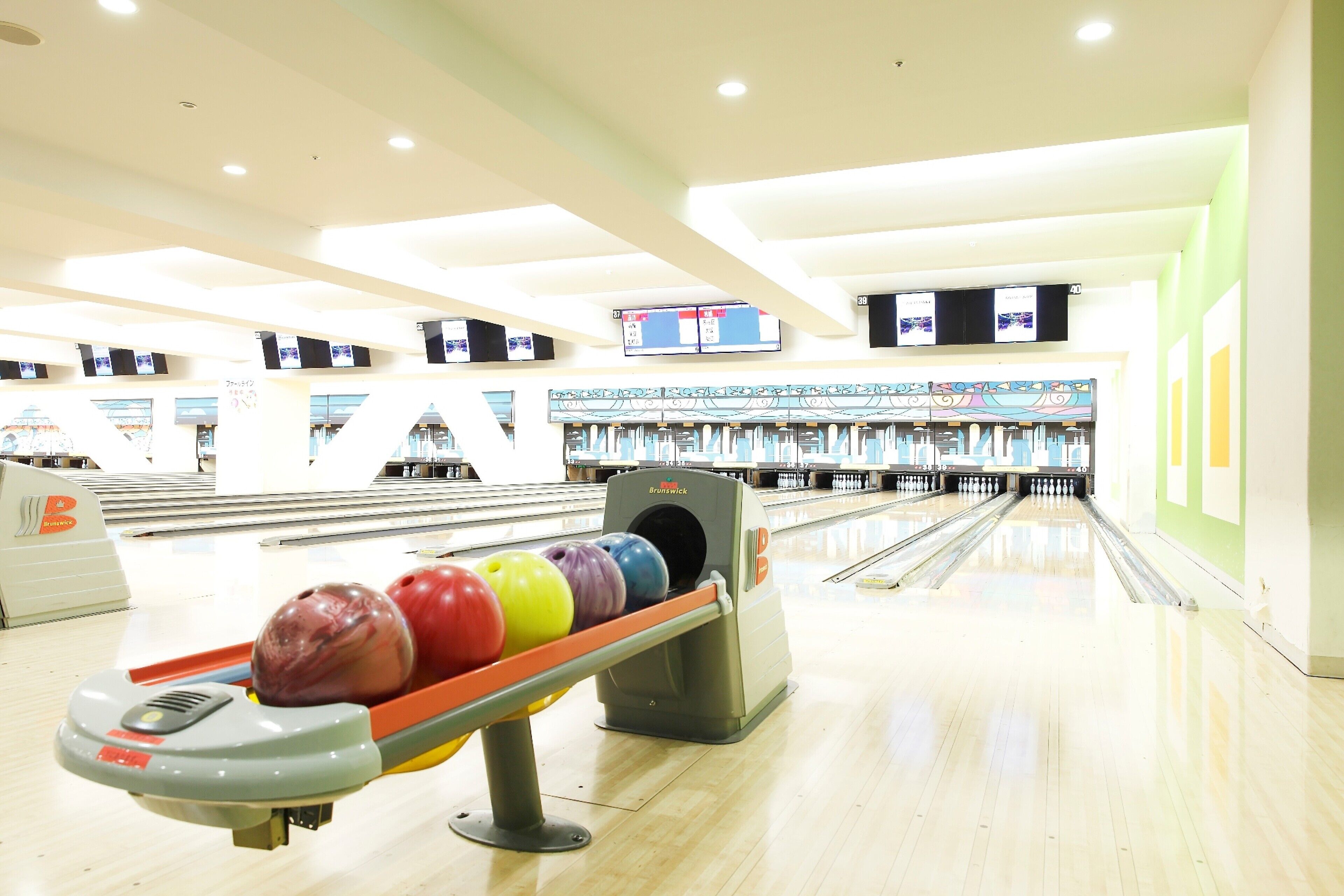 A bowling alley with multiple lanes, a bowling ball return system, and overhead scoreboards.
