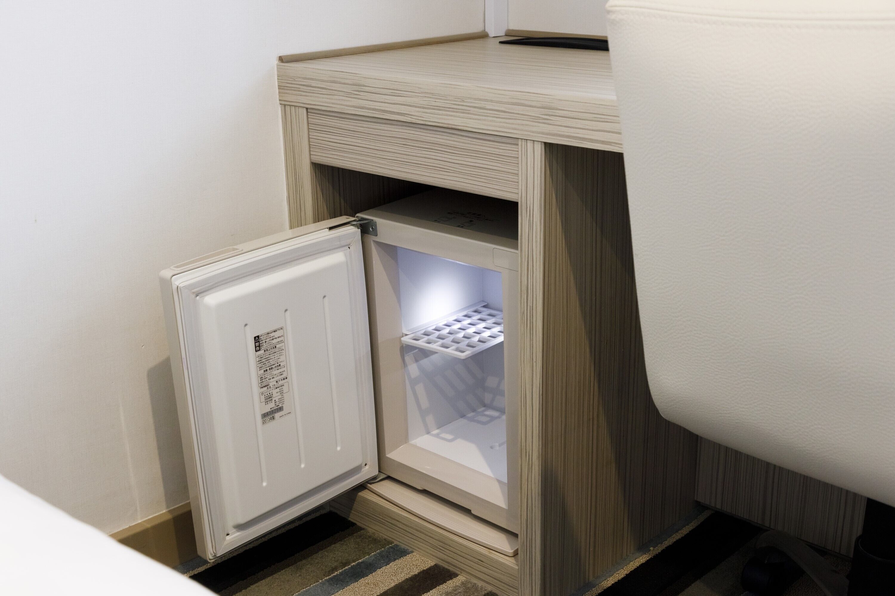 A compact refrigerator with a freezer compartment, situated in a corner of a room with a wooden floor.