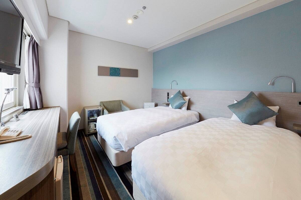 A hotel room with two beds, a desk with a telephone, a television, and a small seating area.