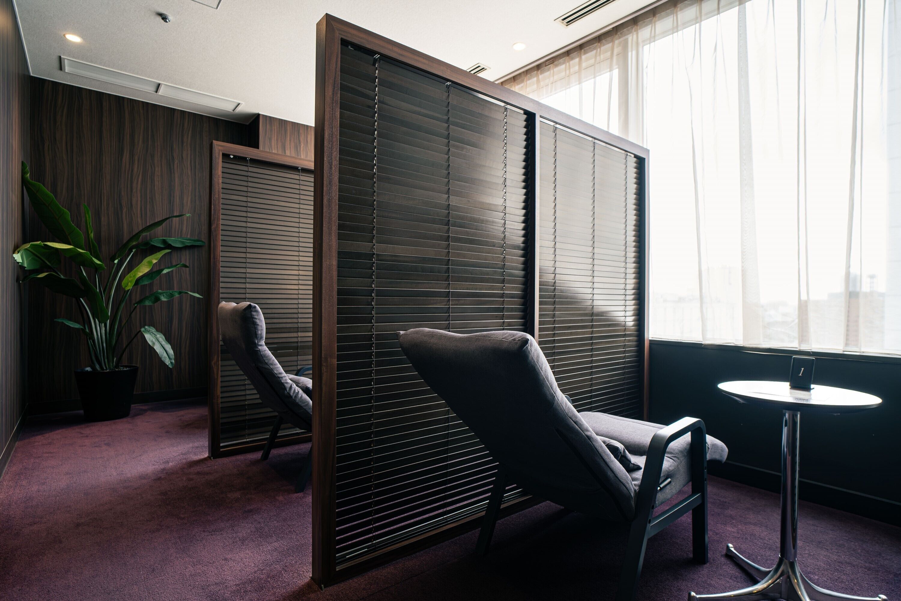 Ein Zimmer mit verschiebbaren Shoji-Schiebetüren, einem gepolsterten Sessel, einem kleinen runden Tisch und einer Topfpflanze.