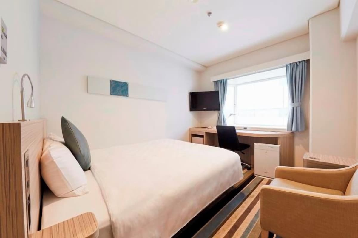 A hotel room with a bed, a desk, a chair, a television, and a window with curtains.