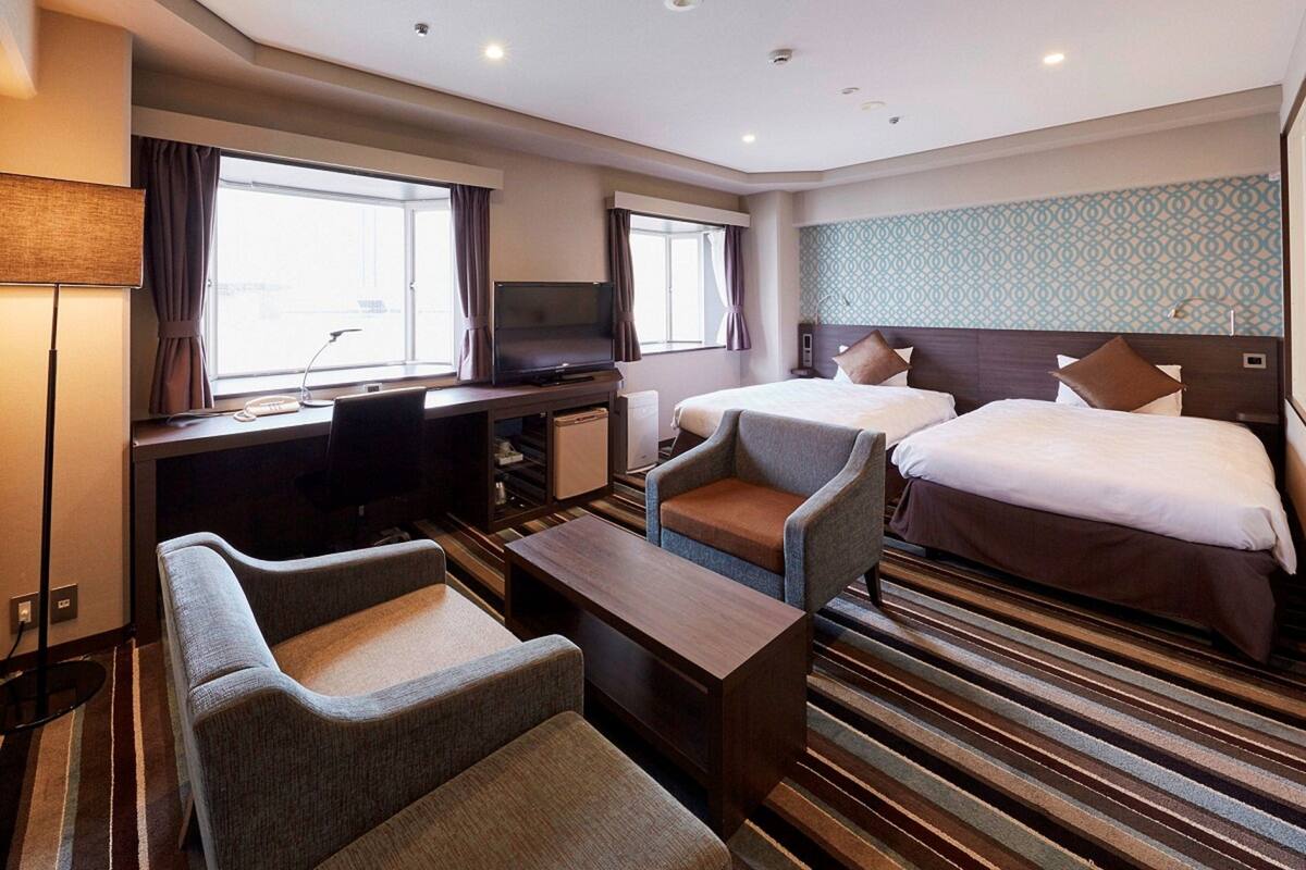 A hotel room with a desk, two beds, a TV, and a seating area.
