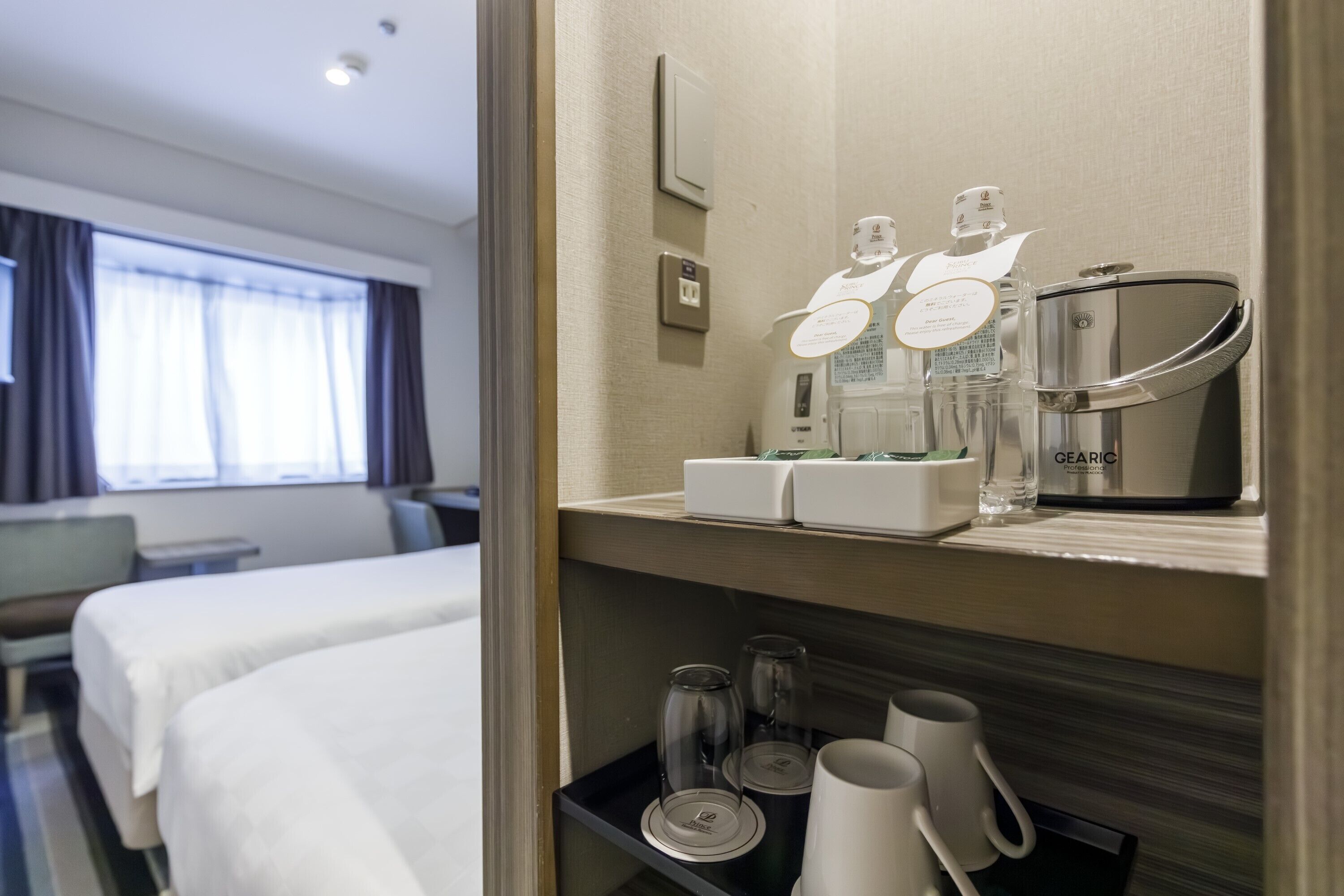 Habitación de hotel con cama, mesita de noche, espejo y repisa con artículos de aseo.