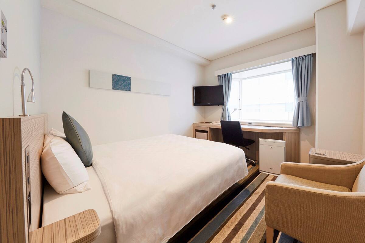 A hotel room with a bed, a desk, a chair, a television, and a window with curtains.