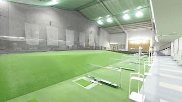 An indoor sports facility with artificial turf, target areas, and a seating area with a staircase.