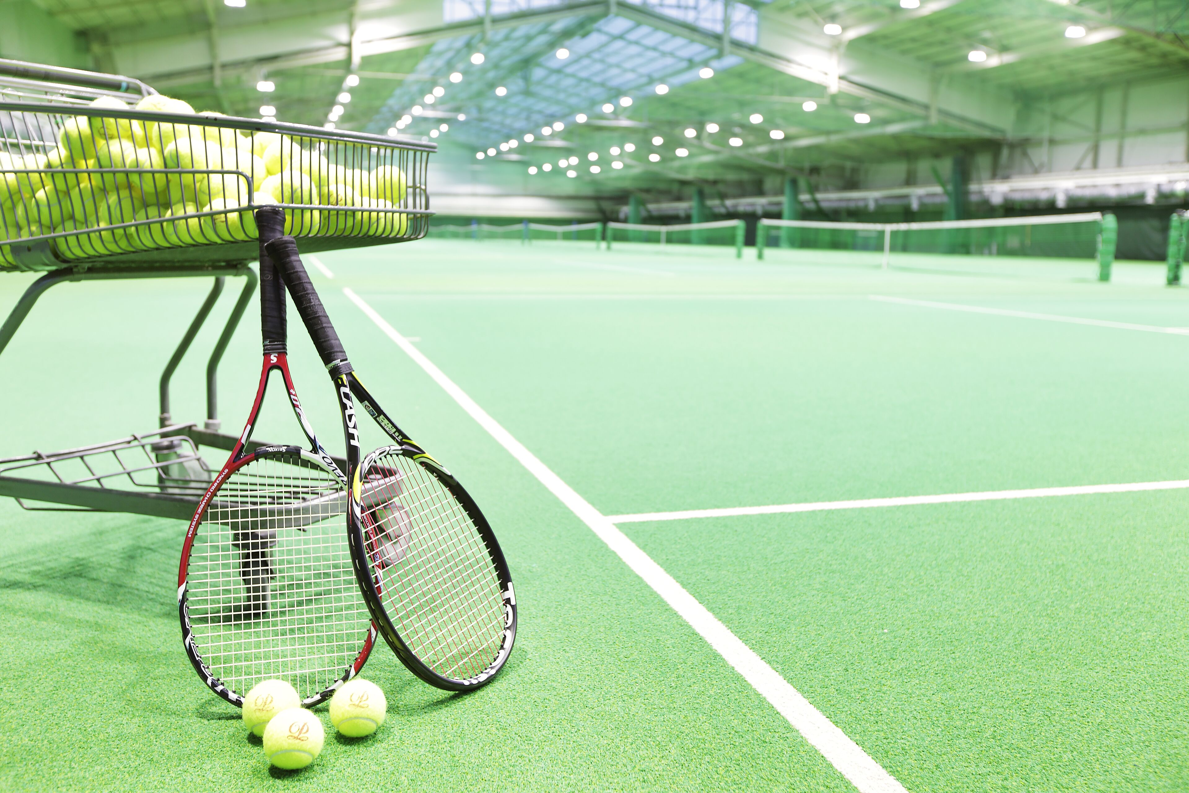A tennis court with a basket of tennis balls and rackets.