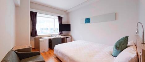 A hotel room with a bed, a desk with a chair, a television, and a window with curtains.