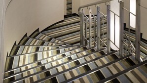 A spiral staircase with metal railings and striped carpet, leading to a room with a window and a door in the background. - Shinagawa Prince Hotel N Tower (Tokyo)