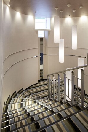 A spiral staircase with metal railings and striped carpet, leading to a room with a window and a door in the background. - Shinagawa Prince Hotel N Tower (Tokyo)