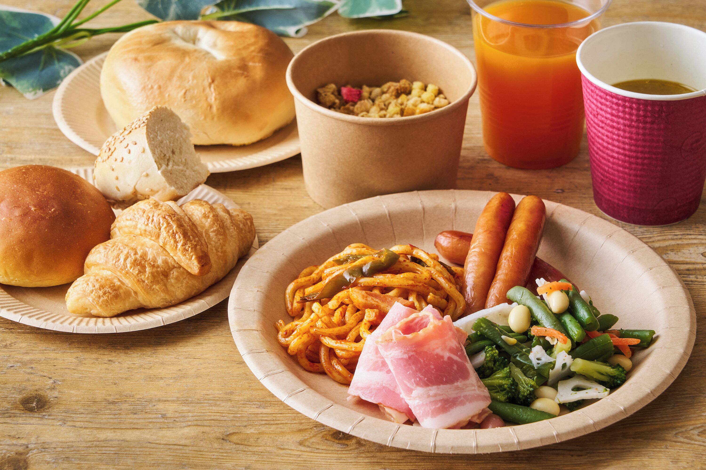 A meal with bread, sausage, vegetables, and a drink on a wooden table.