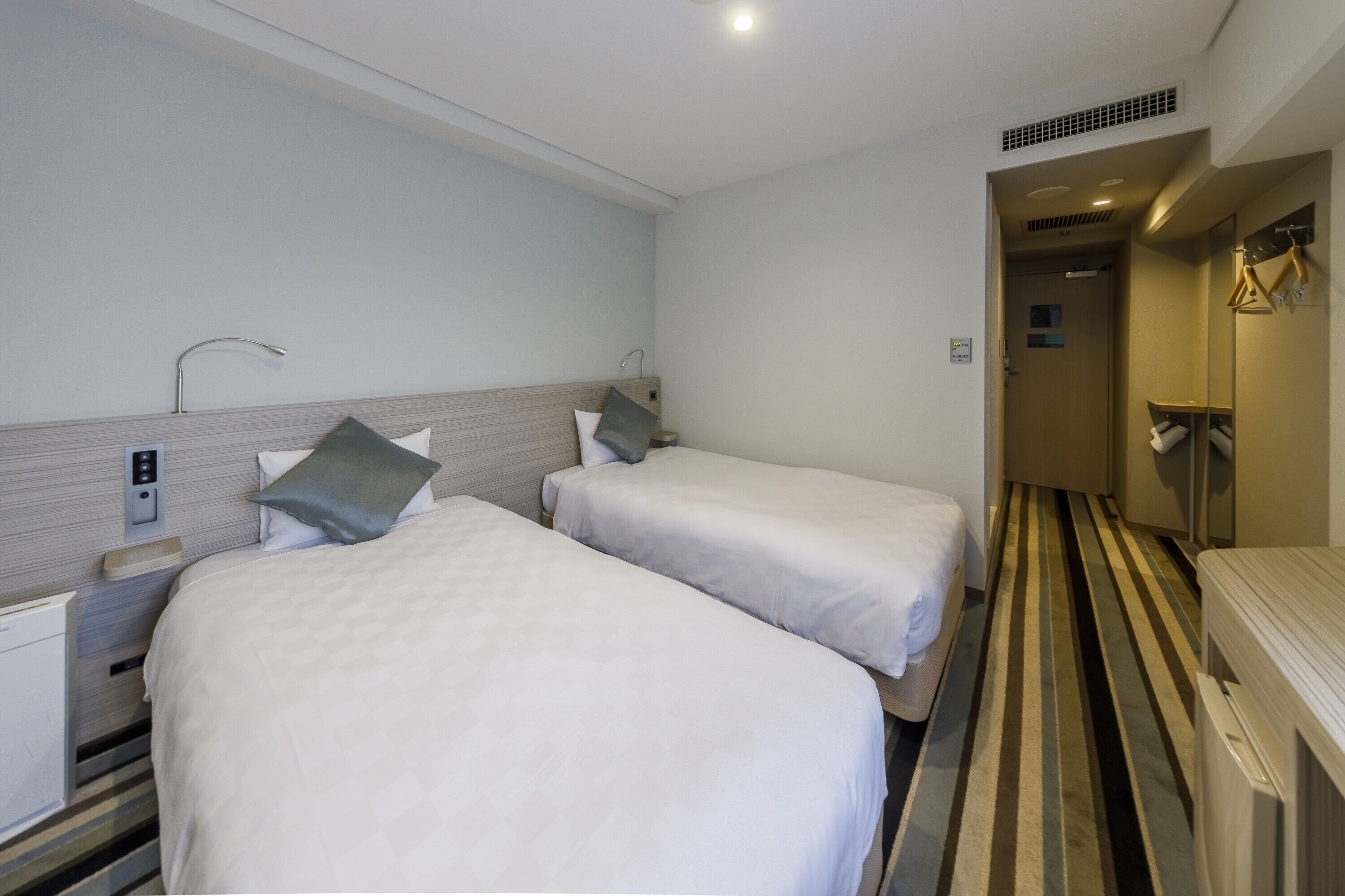 A hotel room with two beds, a bedside table, a mirror, and a striped floor.
