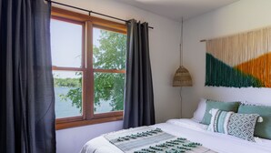Une chambre avec une grande fenêtre, un lit avec une literie verte et blanche, et une décoration murale.