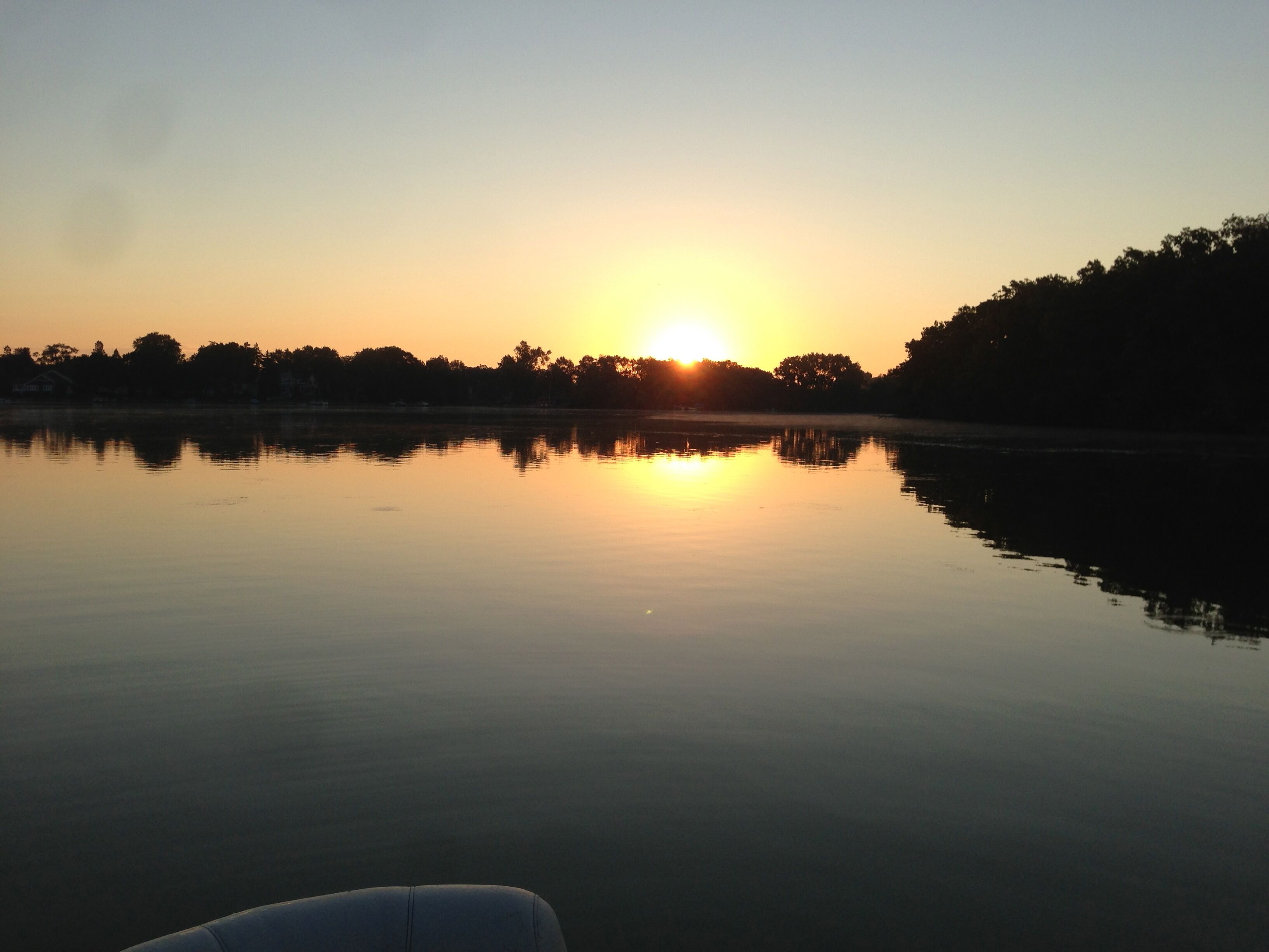 Een rustig meer bij zonsondergang, met een boot op de voorgrond.