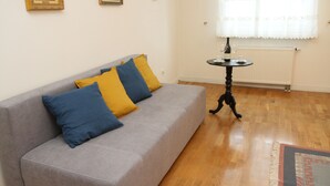 A living room with a grey sofa, blue and yellow cushions, a small round table with a lamp, and a wooden floor. - 270 Pulawska (Warsaw)