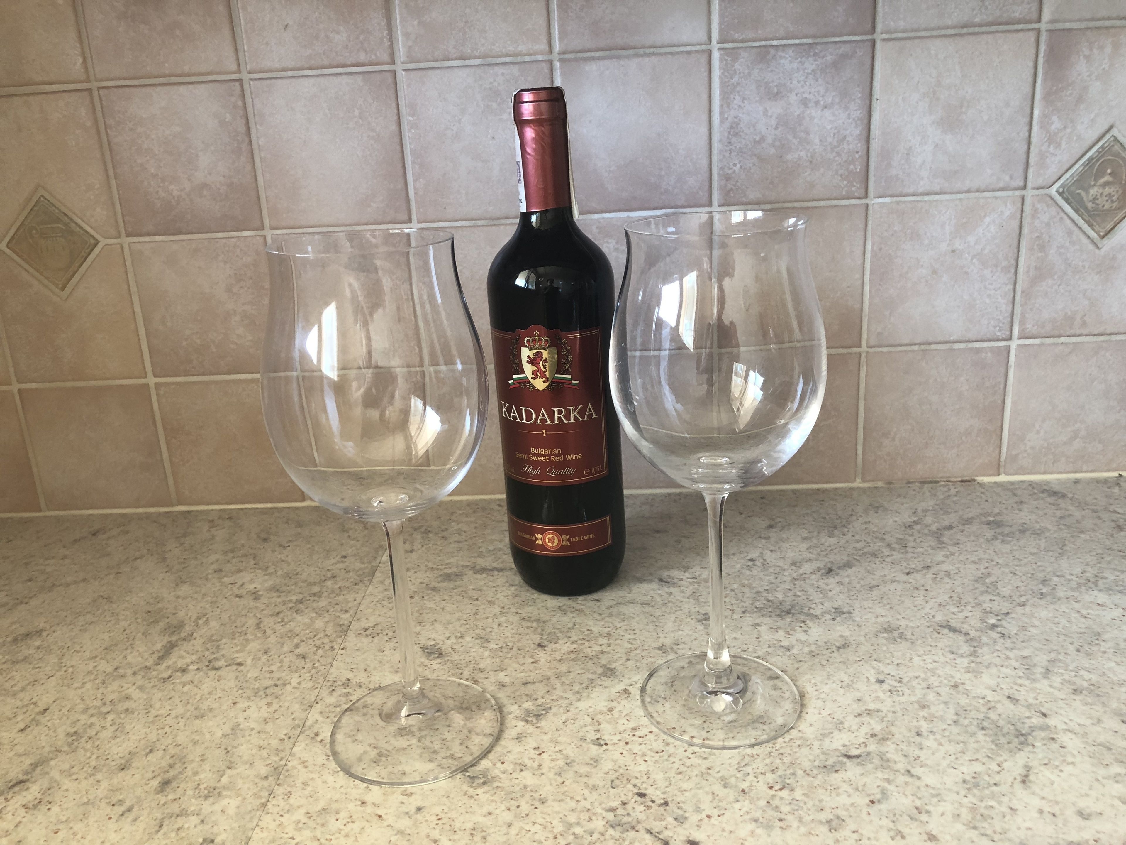 Une bouteille de vin Kadarka et deux verres à vin vides sur un comptoir de cuisine.