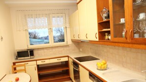 A compact kitchen with a microwave, oven, and sink. There is a table with apples and a bowl of lemons. - 270 Pulawska (Warsaw)
