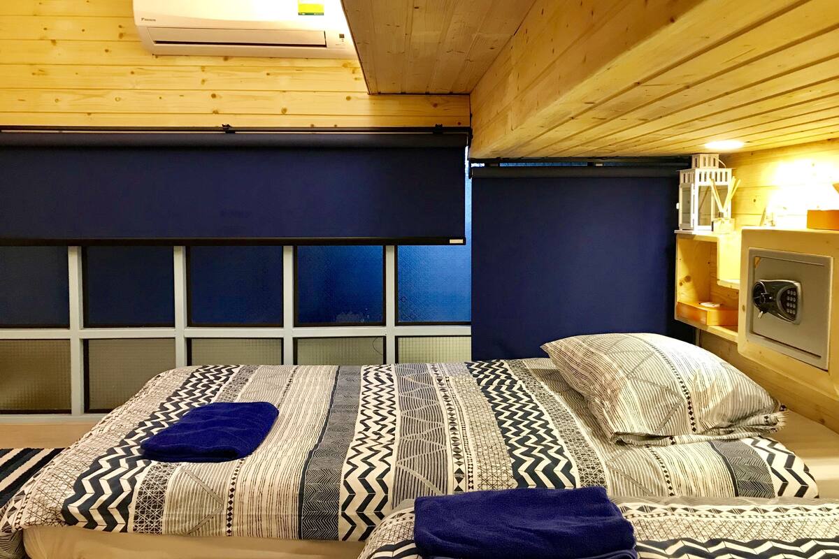 A room with two beds, a wooden ceiling, a window, and a wall-mounted safe.