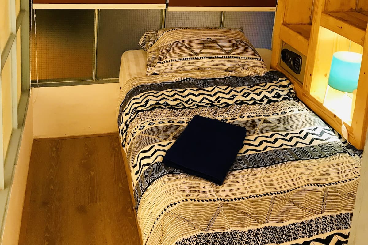 A compact room with a bunk bed, a window with blinds, a bedside table with a lamp, and a wall with a motivational quote.