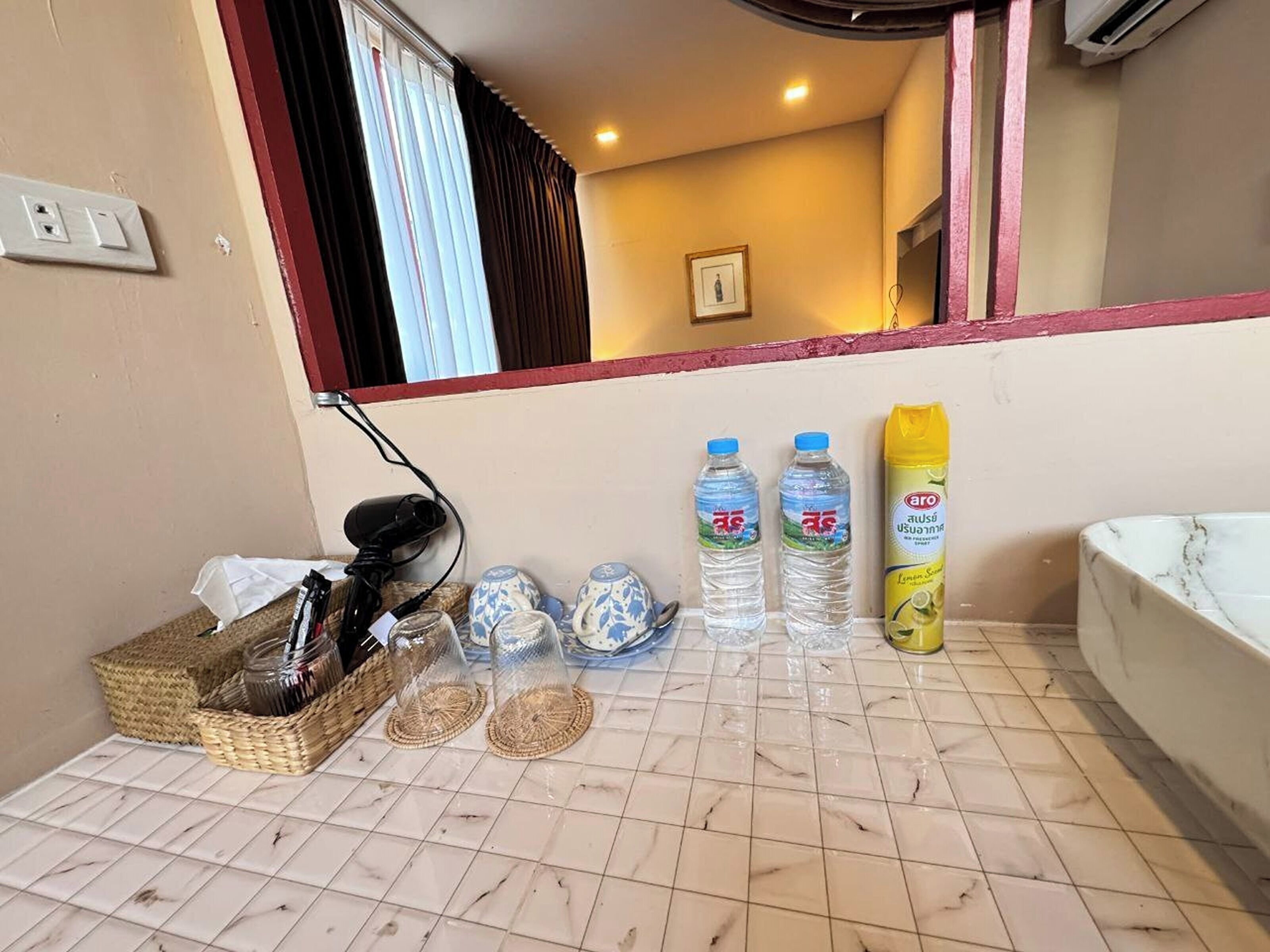 Un baño con bañera, un espejo, una ventana con cortinas y artículos de aseo en el mostrador.