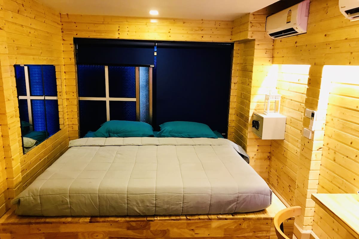 A wooden room with a bed, a window with blinds, and a wall-mounted air conditioner.