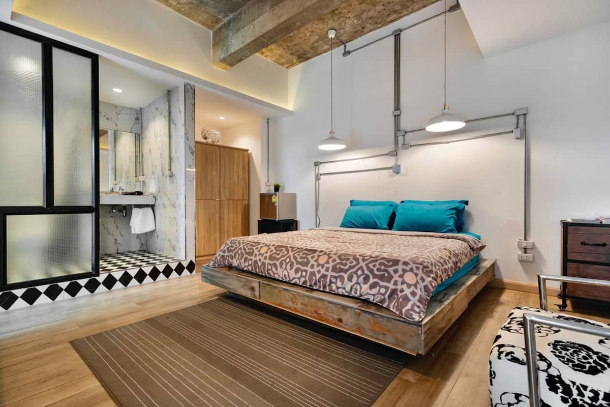 A modern bedroom with a wooden bed, a large window, and a bathroom with a mirror and sink.