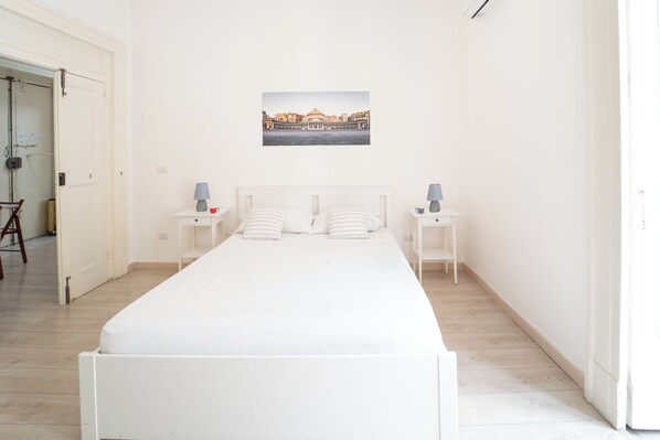 Camera da letto minimalista con un letto singolo, due comodini e un quadro appeso al muro.