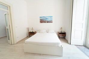 A bedroom with a large bed, two bedside tables, a wall-mounted painting, and a door leading to another room. - Monteoliveto Modern Flat by Wonderful Italy (Naples)