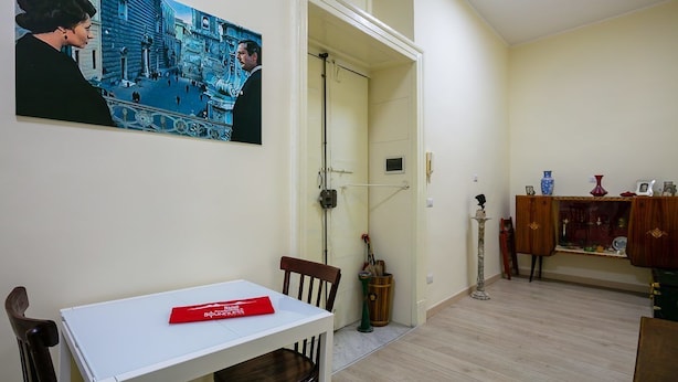 Ein Zimmer mit einem weißen Tisch, einem Stuhl, einem Bild, einer Tür, einem Schrank und einer Stehlampe.