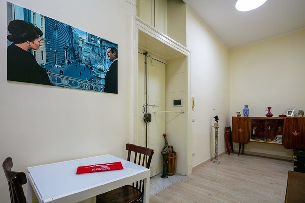 A room with a white table, a chair, a painting, a door, a cabinet, and a floor lamp. - Monteoliveto Modern Flat by Wonderful Italy (Naples)