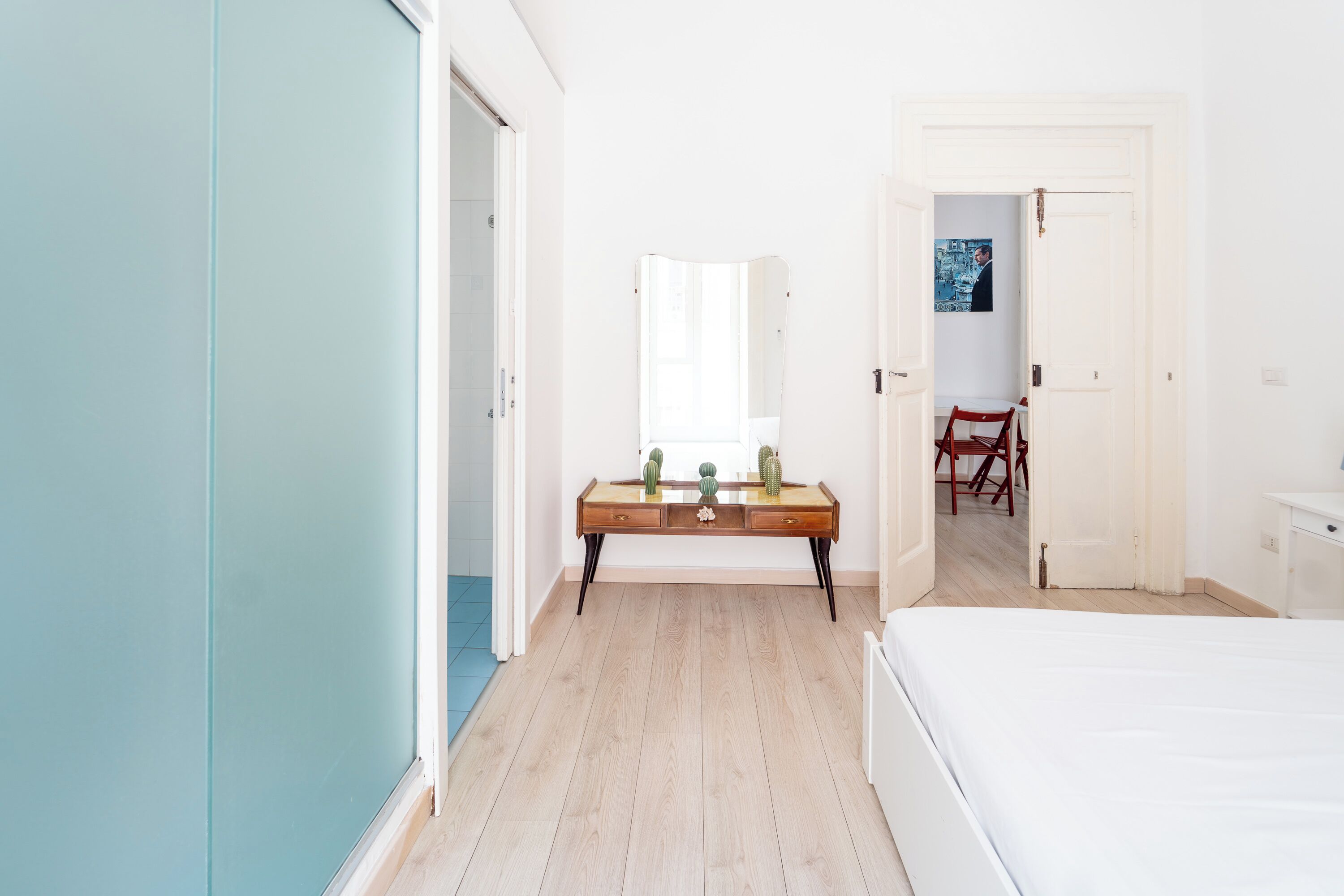A bedroom with a bed, a wooden dresser, a mirror, and a dining area with chairs and a table.