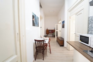 Un corridoio stretto con zona pranzo, tavolo e sedie, forno a microonde e credenza con stoviglie.