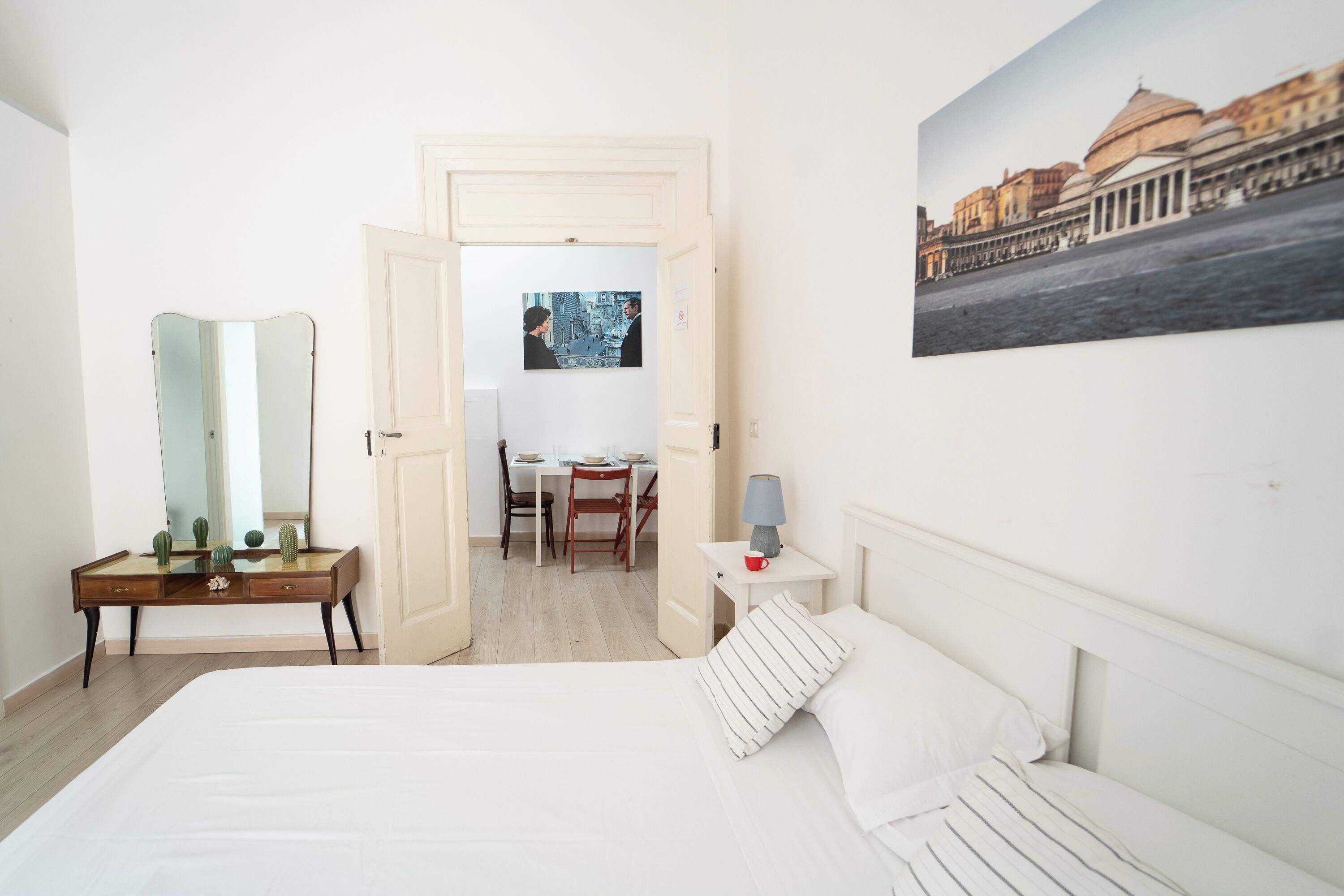 A hotel room with a bed, a desk, a chair, a lamp, and a painting on the wall.