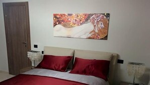 Een slaapkamer met een bed, een houten deur, een nachtkastje en een schilderij aan de muur.