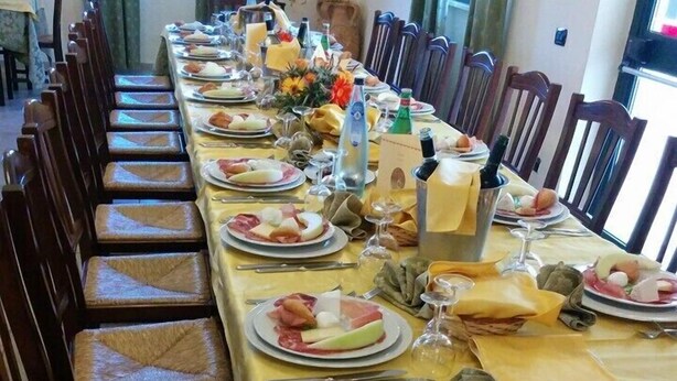 Een lange eettafel gedekt met borden eten, glazen en bestek, omringd door houten stoelen.