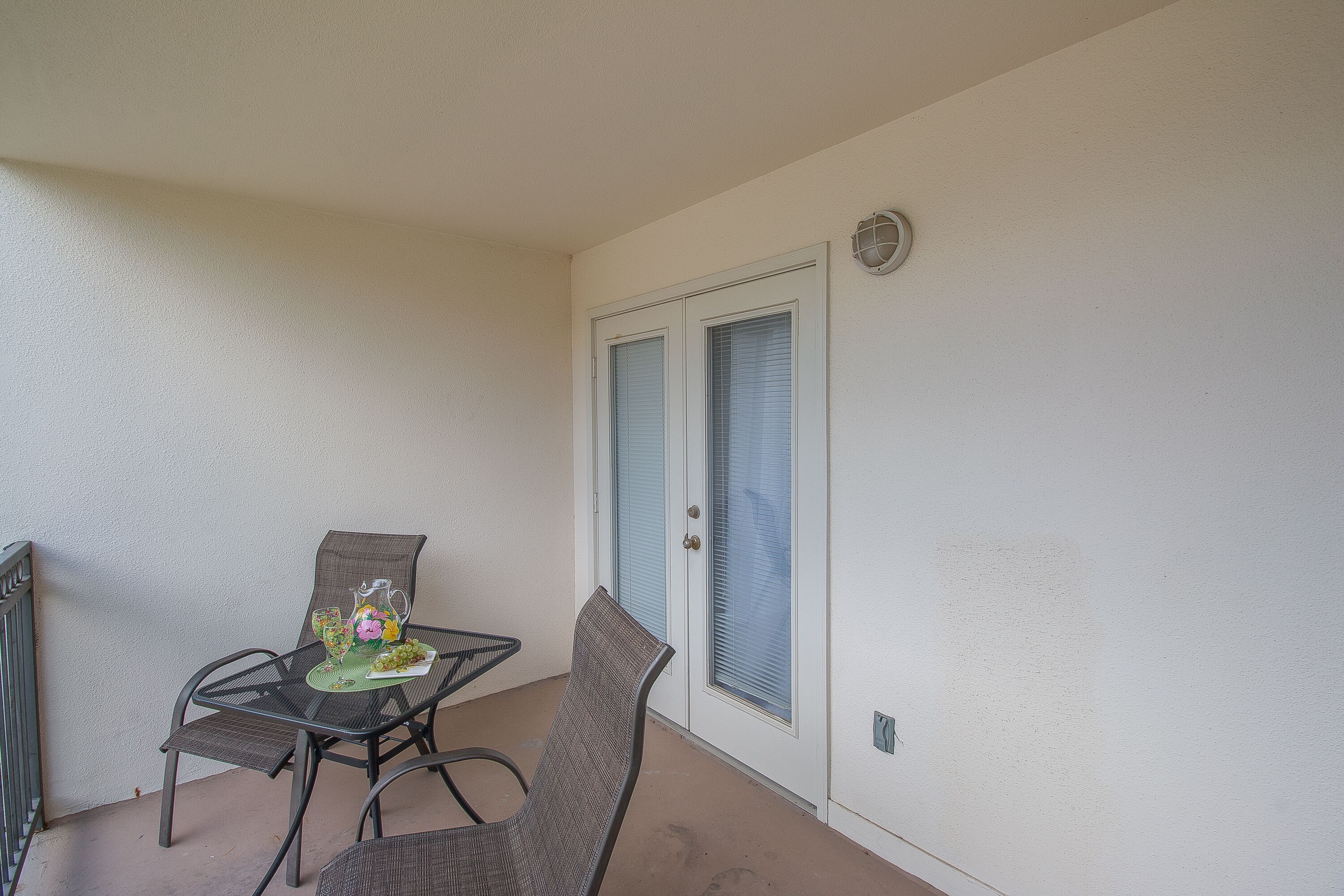 Ein Balkon mit Tisch und Stühlen, eine Tür mit Milchglasfenstern und ein kleines dekoratives Element auf dem Tisch.