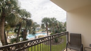 Un balcon avec vue sur une piscine, des palmiers et des chaises longues.