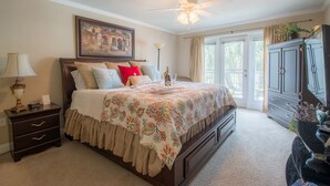 Une chambre à coucher avec un grand lit, un ventilateur de plafond, une table de chevet, une commode et une fenêtre avec des rideaux.